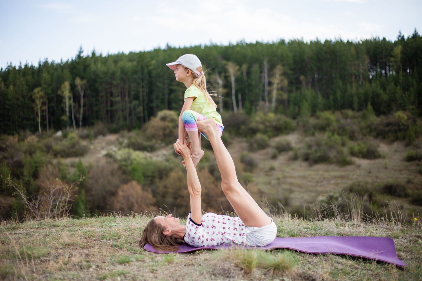 Een moeder en dochter doen samen een duo-yogahouding op een yogamat in de natuur